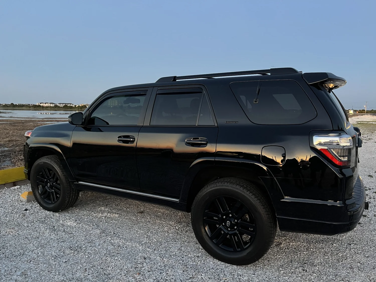 Owner's black 4Runner beside the coast at sunset, reflections visible along its paintwork